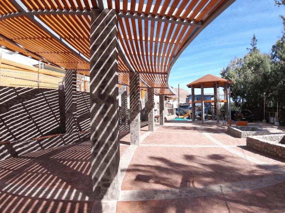 Obra terminada: pérgola de madera y estructura de piedra en una plaza pública